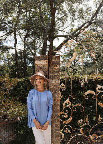 Outdoor shot of a woman wearing a long sleeve blue top, white pants and a sunhat (Product image)