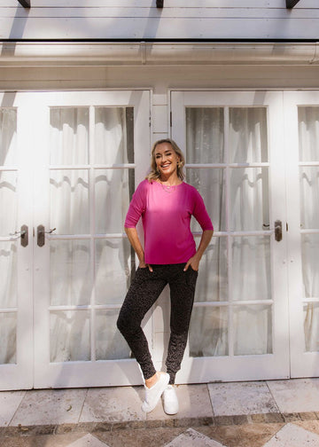 Outdoor shot of a woman wearing a pink 3/4 sleeve top, black fitted pants and white sneakers (Product image)