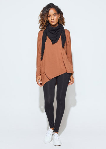 A full body shot of a woman wearing a black scarf over a rust coloured long sleeve top, black leggings and a white sneakers