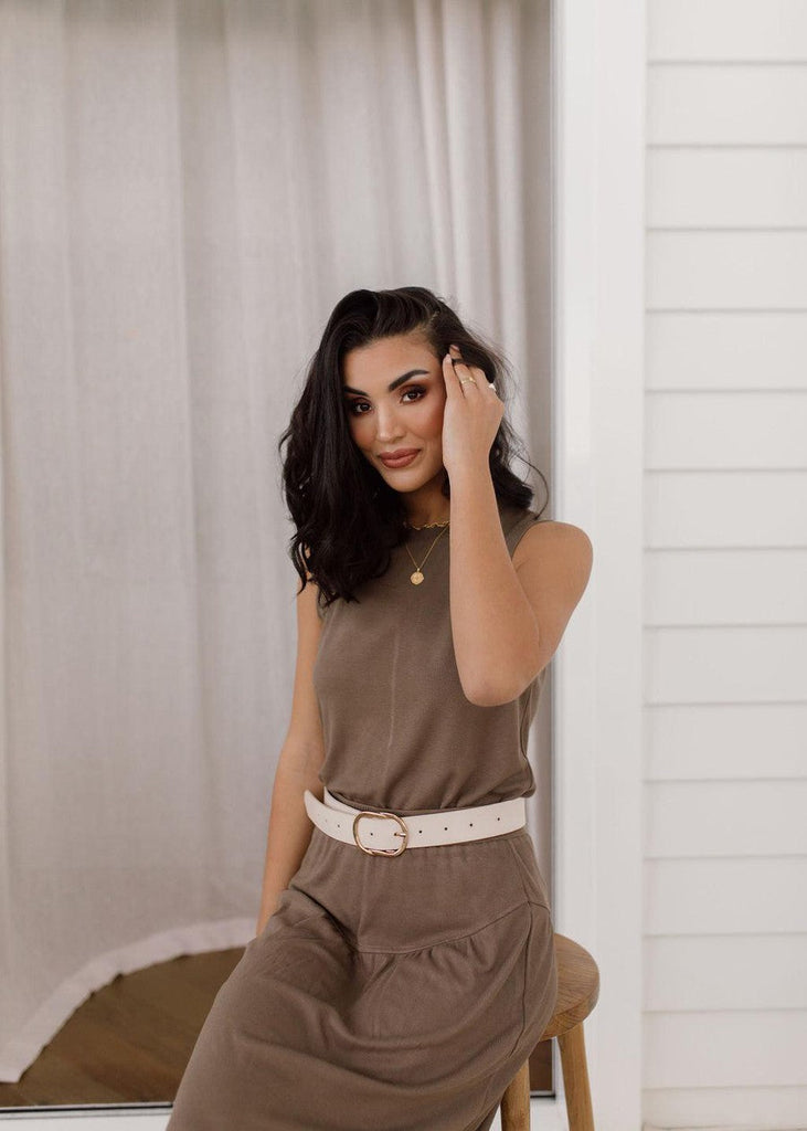 A close up pictorial of a woman wearing a sleeveless brown midi dress with a white belt. Adding an accessory to the simple dress made it look sophisticated