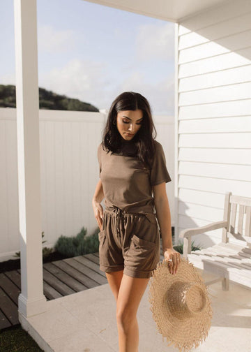 Outdoor shot of a woman wearing brown top and short set while holding a sunhat in her left hand (Product image)