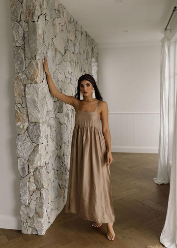 A woman posing beside a rock wall wearing a bronze sleeveless maxi dress, taken indoors (Product image)