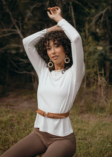 A woman wearing a white long sleeve bamboo top and a brown fitted pants in an outdoor setting (Featured image)