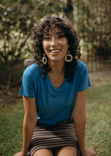 A model smiling with a curly hair while wearing a blue top and striped brown & black skirt (Product image)