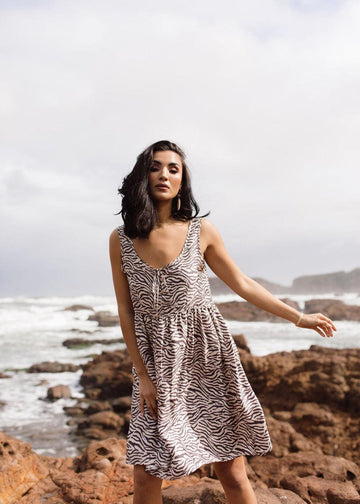 A woman wearing a sleeveless animal printed silk dress with the photo taken outside, with a beach background