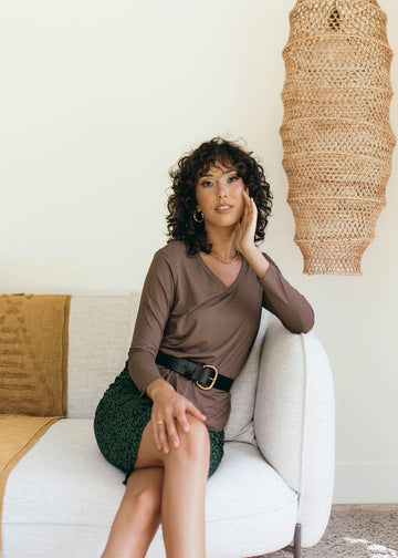 A pictorial of a woman sitting comfortably in a couch, wearing a brown long sleeve top and a printed midi skirt