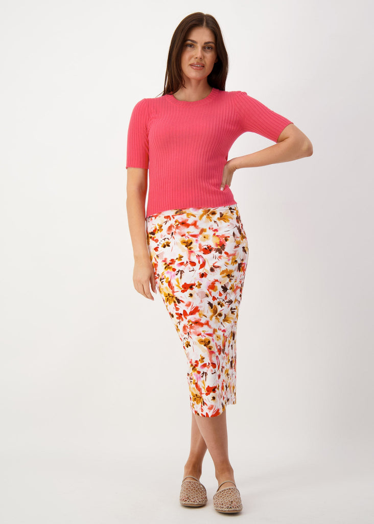 A woman posing with her hand in her waist while wearing a fitted top, floral midi skirt & brown flat sandals (Product image)