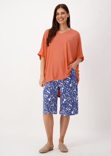 A woman modelling Lou Lou's Orange Slouch Bamboo Tee partnered with a floral blue shorts