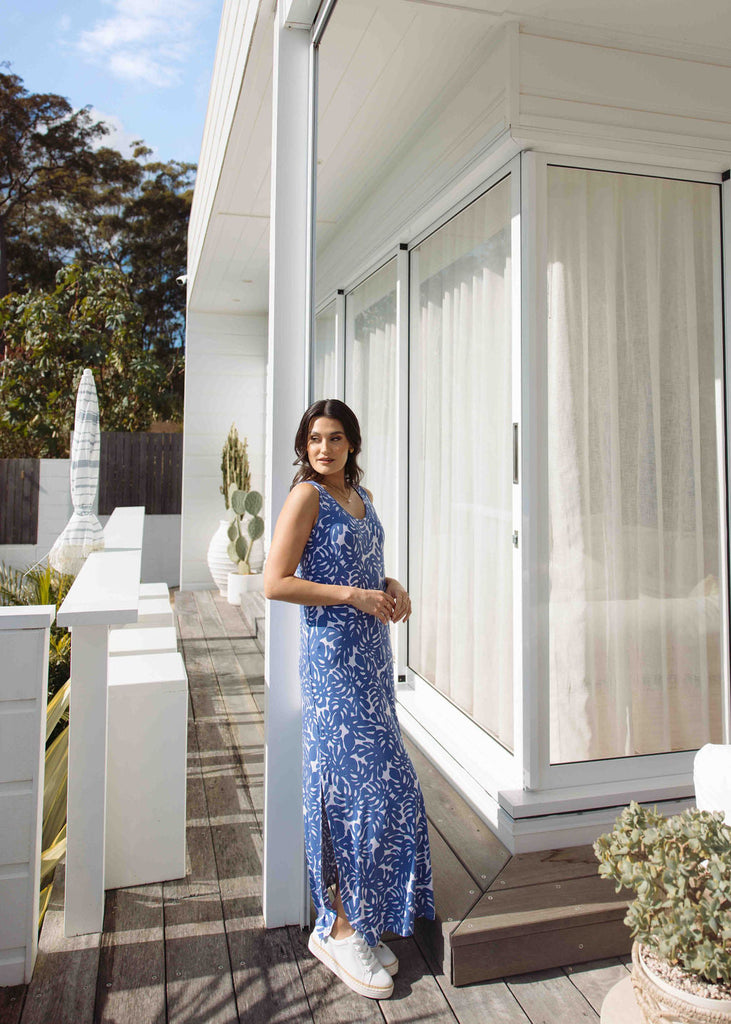 A woman posing outside while wearing Lou Lou's Printed Navy Blue Long Dress matched with a white sneaker