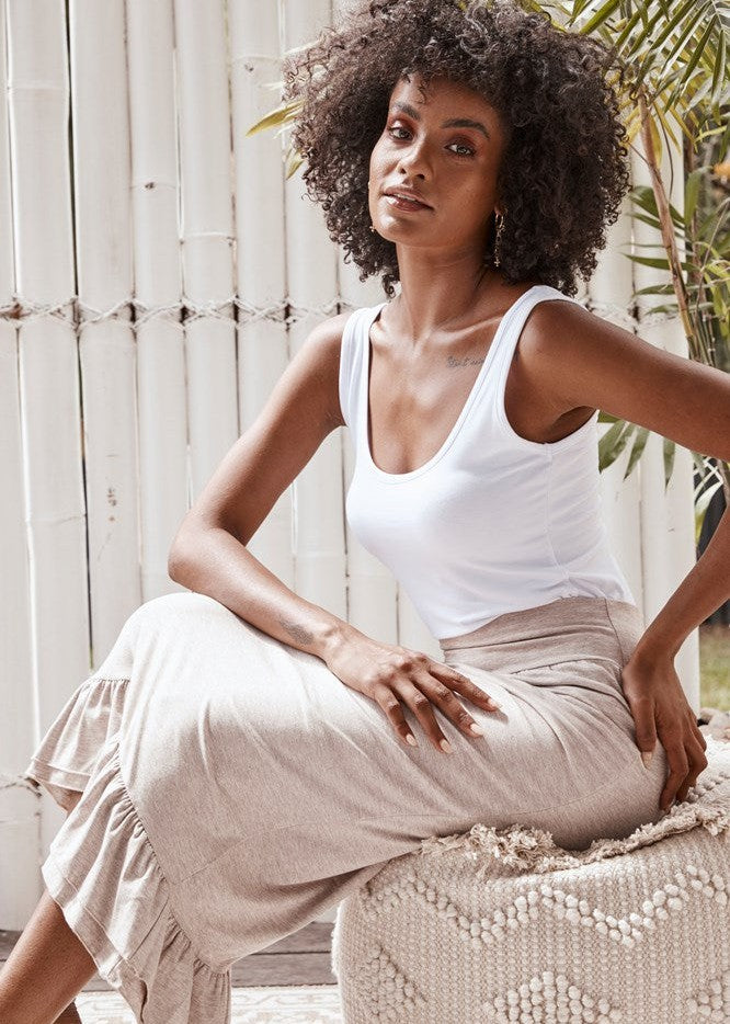 A beautiful black woman sitting in a decorative chair while wearing a white bamboo singlet and cream coloured midi skirt