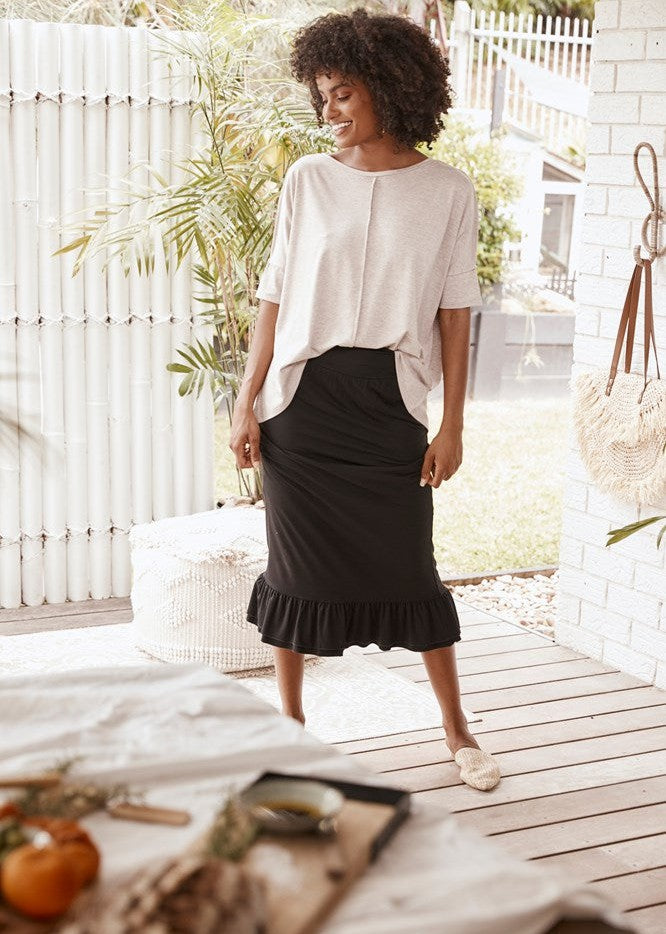 A beautiful black woman with curly hair wearing a white oversized bamboo tee, black midi skirt and a white flat sandals