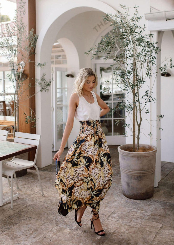 An outdoor pictorial of a woman wearing a white sleeveless top and printed maxi skirt and black strap high heel sandals