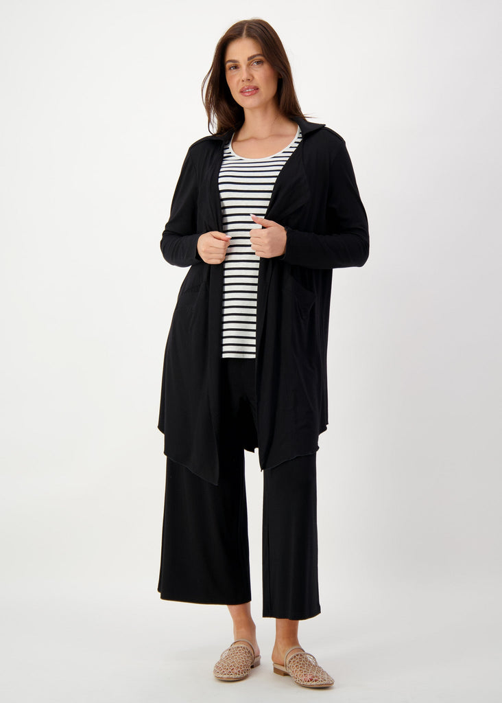 A woman wearing a black bamboo trench coat over a striped top, relaxed black pants & brown sandals (Product image)