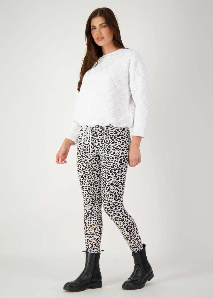 A woman posing in a grey backdrop wearing a white pullover, an animal printed full-length bamboo leggings and a black boots (Product image)