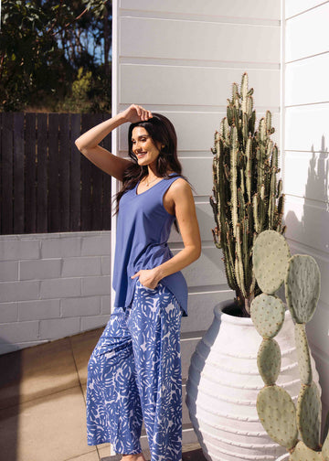 A woman posing beside a cactus plant taken outdoor while wearing a marlin blue v-neck bamboo tank top and printed pants (Product image)