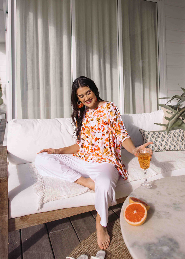 A woman sitting comfortably in a sofa in the porch, wearing an oversized floral slouch tee and white pants (Product image)