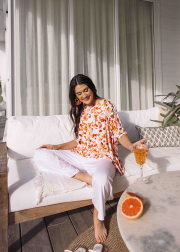 A woman sitting comfortably in a sofa in the porch, wearing an oversized floral slouch tee and white pants (Product image)