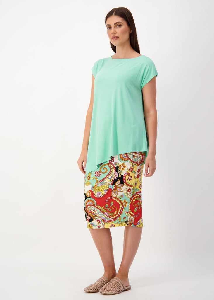 A woman standing in grey backdrop wearing a turqoise asymmetrical bamboo t-shirt, printed midi skirt and a brown flat sandals (Product image)