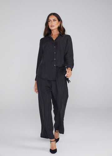 A confident woman wearing a black bamboo long sleeve button down top and a black pants matching with a pair of black pointed heels