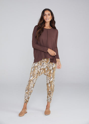 A woman with long brown curly hair wearing an brown long sleeve top and printed pants. It gives off a good combination or plain and printed clothing style