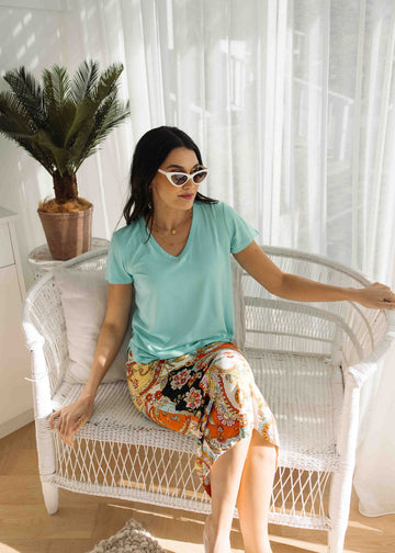 A woman sitting in ratan chair while wearing a sunglass, bamboo v-neck tshirt and a printed midi skirt (Product image)