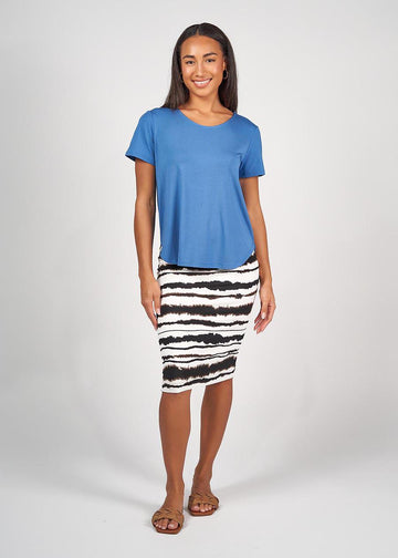 A beautiful woman smiling while wearing a blue bamboo tee, a printed black and white midi skirt and a pair of brown sandals