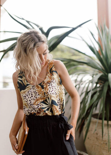 A beautiful blonde girl wearing patterned sleeveless bamboo top and black pants